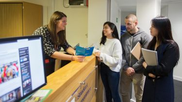 Three students getting assistance from a member of staff at the Students at the Student Experience Office