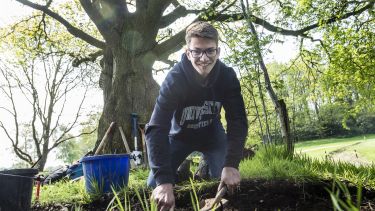 An archaeology student at a dig site in a wooded area.