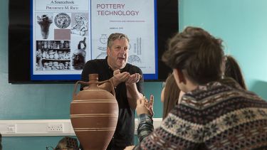Students listen whilst a lecturer delivers a talk on pottery analysis.