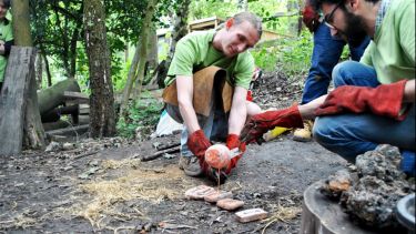 Two archaeology students recreating prehistoric metallurgy in a woodland environment.