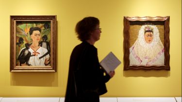 Someone looking at two paintings of Frida Kahlo.