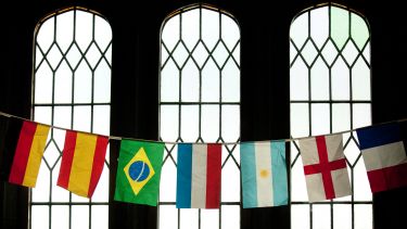 A line of different countries' flags hung up in front of a window