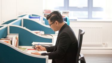 Postgraduate student sat at a desk studying.