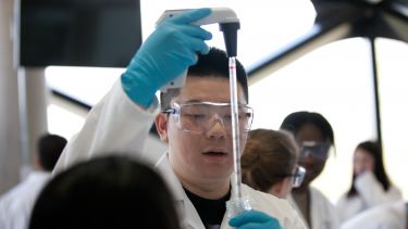 A student carrying out an experiment in The Diamond. He has blue gloves and a lab coat on. 