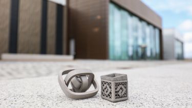 A modern building in the background, metal 3D-printed objects in the foreground