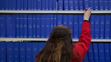 A female student selecting a book from the Health Sciences library. All of the books are blue. 