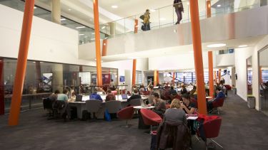 A large student study space in The Diamond. There are multiple students working. There are orange beams around the space.