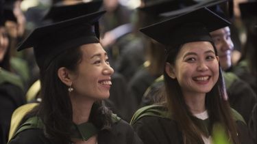 Two female students laughing in their graduation ceremony. 