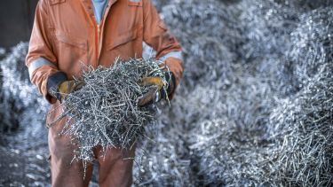 A person in orange protective clothing and gloves holding a handful of metal machining waste