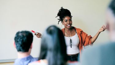 Teacher stood at the front of a class teaching English.