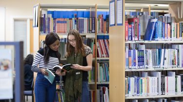 Two female students from the School of Health and Related Research take a look at the content of library books.