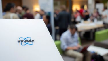 A Bruker logo in the foreground with networking people in the background