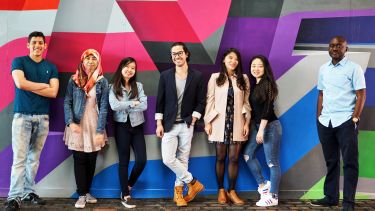 A group of international student ambassadors stand against a colourful wall. 
