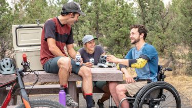 A group of people sit on a picnic bench; one of them is a wheelchair user.