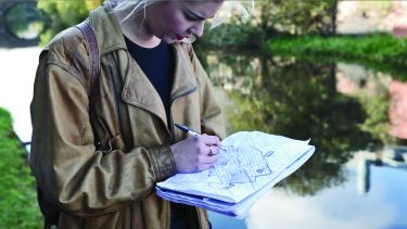 Student writes notes on map in front of canal