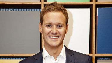 Journalism alumni Dan Walker. He is smiling and standing in front of some colourful blocks. 