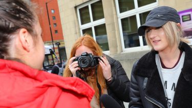 Two journalism students interviewing a member of the public, using a camera and mic