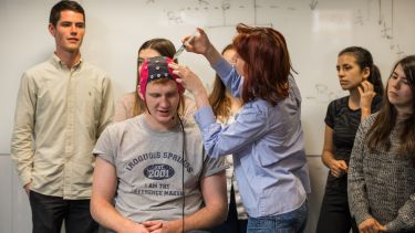 Lecturer demonstrating an EEG is a test to a class. A student wears a headpiece used to evaluate the electrical activity in the brain