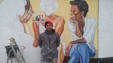 Italian muralist Jupiterfab stands against a half-finished mural of women talking