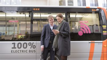 Man and woman stood in front of an electric bus looking at the woman's phone