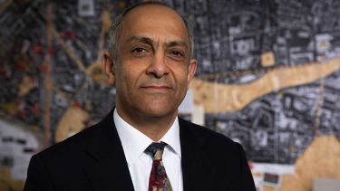 A photo of Professor Karim Hadjri stood in front of architectural drawings - image