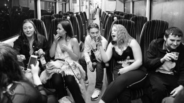 Black and white photo of young people talking and drinking in an empty train carriage