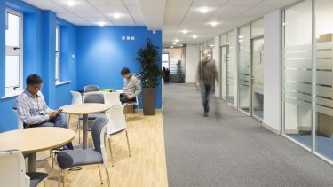Two people relaxing at tables in Mappin Street and someone else walking along the corridor past them.