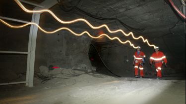 Researchers  walking through an underground tunnel at Boulby Underground Laboratory. Lightwaves coming from their head torches are visible