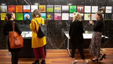 An image of visitors looking at display cases of a Library exhibition.