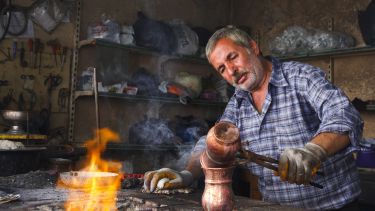 A man pours hot liquid into a pot next to an open fire