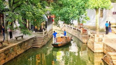 A small boat on a little river going through an urban area in Suzhou, china