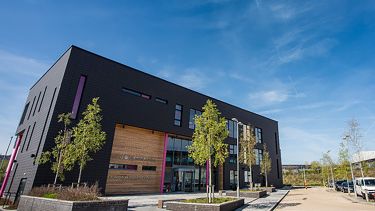 The outside of the Knowledge Transfer Centre building, a rectangular grey building with a car park.