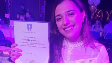 Andra-Maria smiling, at her graduation after-party, holding her certificate