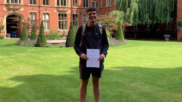 Chris standing in the courtyard at Firth Court, smiling and holding a certificate