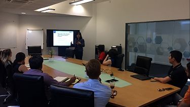 Dr Gate Pichawadee Kittipanya-ngam giving a talk in front of a screen to a group of people sat around a table.