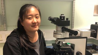Ge Zhang working with a microscope in the lab