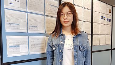 Xiaowen Gu stood smiling in front of a pin board, smiling