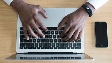 Picture of a person's hands typing on a laptop with a mobile phone on the desk.