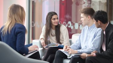 Four students sitting in armchairs with books having a conversation