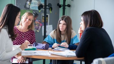 One student is speaking while the tutor and fellow students listen