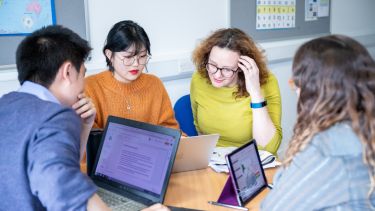 Three students using computers or tablets sit with a tutor