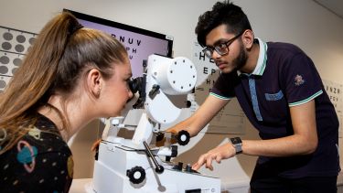 Orthoptics Student testing eyes of female student with retina equipment