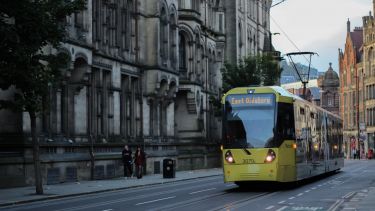 Tram goes past old building in Manchester