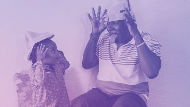 Picture of a girl and older man smiling, wearing paper hats. The image has a purple filter. 