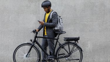 Man with an ebike stood by a concrete wall looking at his phone