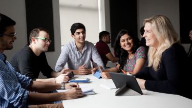 5 students sitting around a desk doing group work in a seminar room