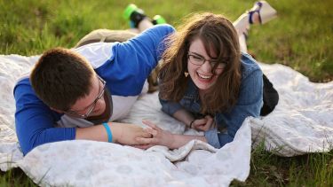 Two people laughing and lying on a blanket in park