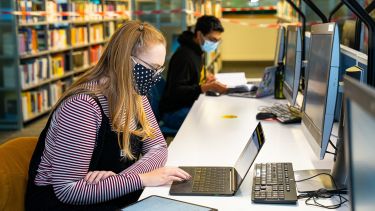 Student wearing a protective mask and studying at a laptop in Weston Park library
