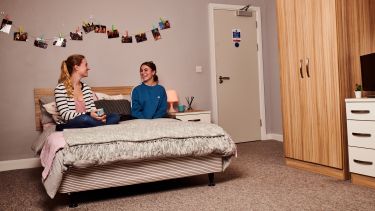 two students sat on a double bed talking