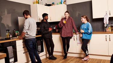 Four students stood in a kitchen laughing and drinking tea